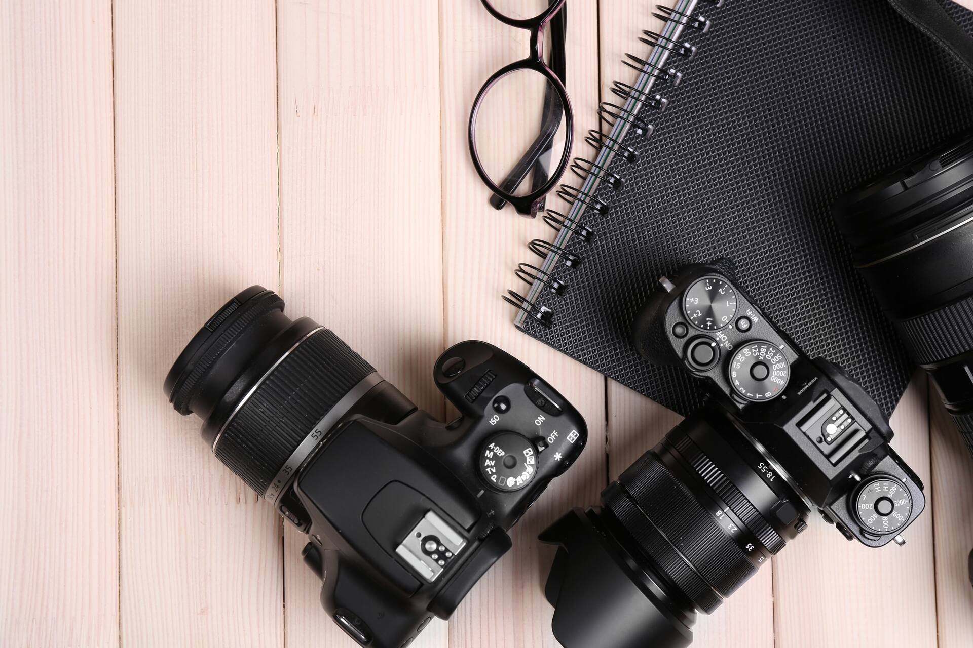 Dos cámaras de fotos junto a un cuaderno y unas gafas